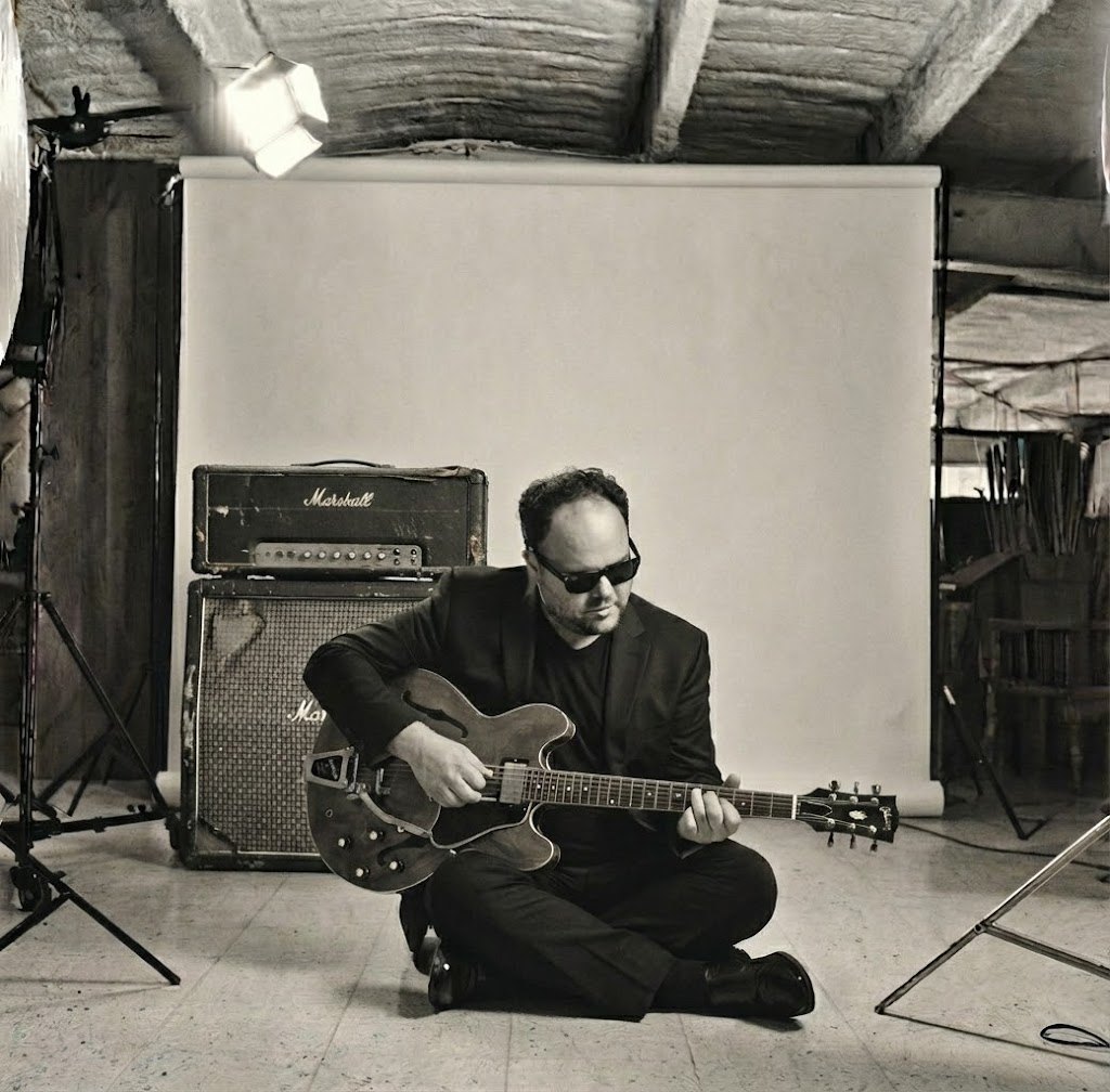 Chuck Credo IV seated with his black Fender Stratocaster